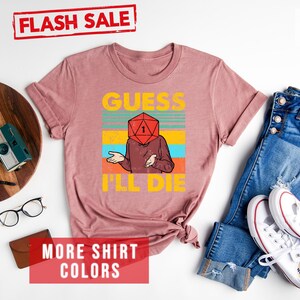 May include: A heather mauve t-shirt with a retro-style graphic of a person with a dice for a head. The text on the shirt reads "Guess I'll Die".