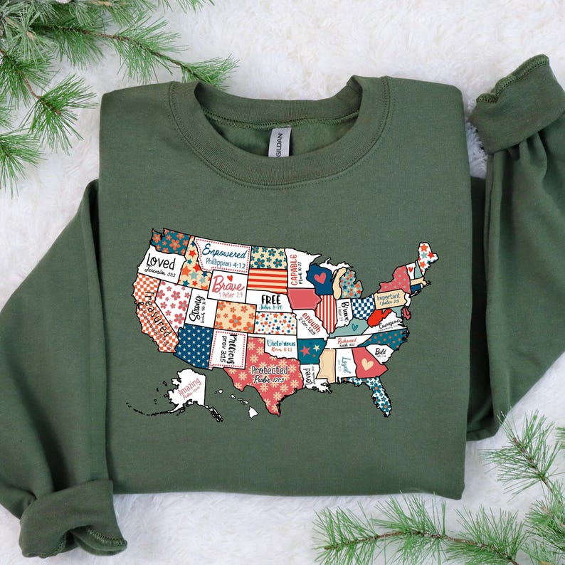 May include: Green sweatshirt with a patchwork design of the United States featuring inspirational words and bible verses. The words include "Loved", "Empowered", "Brave", "Free", "Strong", "Protected", "Capable", "Enough", "Amazing", "Faithful", "Bold", "Hope", "Joy", "Peace", "Love", and "United".