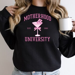 May include: Black sweatshirt with pink text that reads "MOTHERHOOD UNIVERSITY EST. 1989" and a pink martini glass with pink berries on top.