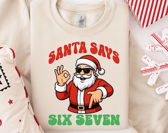 May include: A cream-colored sweatshirt with a graphic of Santa Claus wearing sunglasses and giving an 'okay' hand gesture. The text "SANTA SAYS" is above the Santa graphic in red, and "SIX SEVEN" is below in green.