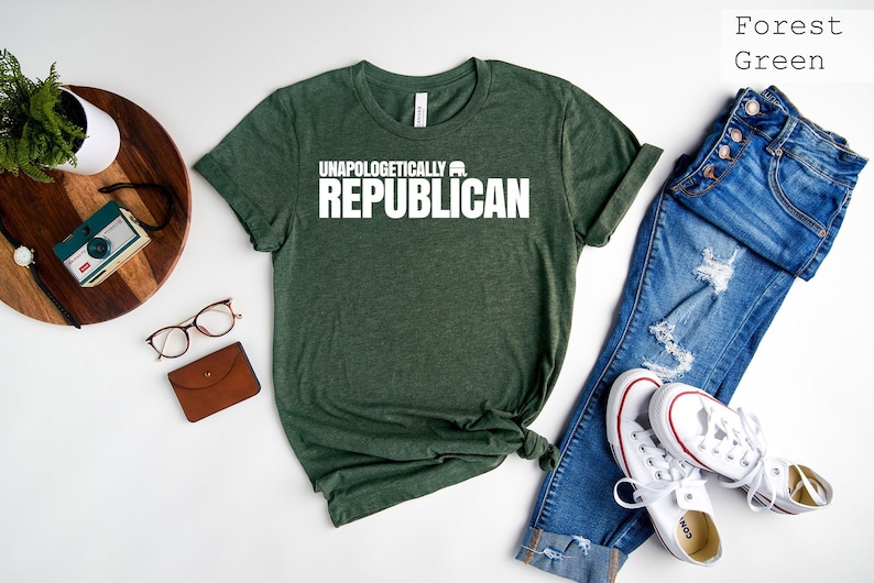 May include: Forest green t-shirt with the text "Unapologetically Republican" in white. The shirt is laid flat on a white surface with a pair of jeans and white sneakers.