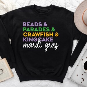 May include: Black sweatshirt with the text "BEADS & PARADES & CRAWFISH & KINGCAKE mardi gras" in colorful letters.