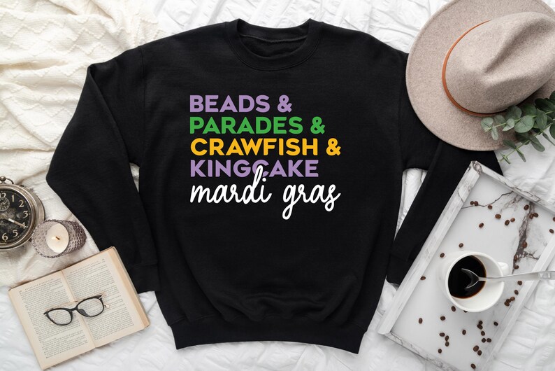 May include: Black sweatshirt with the text "BEADS & PARADES & CRAWFISH & KINGCAKE mardi gras" in colorful letters.