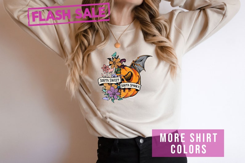 May include: Beige sweatshirt with a pumpkin graphic. The pumpkin is half orange and half floral, with a bat wing and the text "Sorta Sweet Sorta Spooky". A pink "Flash Sale" banner is at the top.
