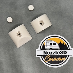 Op de afbeelding: Off-white 3D-geprinte caravanonderdelen en twee kleine ronde stukken worden getoond op een grijze ondergrond. Een sticker met de tekst "Nozzle3D Caravan" en een caravan-afbeelding is ook aanwezig.