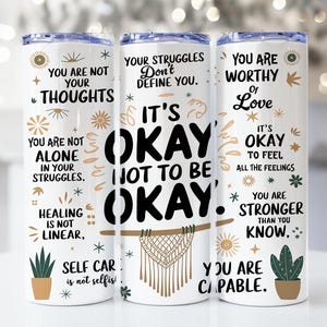 Puede incluir: Tres vasos blancos con citas y diseños inspiradores. Los vasos presentan citas como "No eres tus pensamientos", "Está bien no estar bien", y "Eres digno de amor".