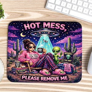 Puede incluir: Alfombrilla de ratón colorida con una ilustración de dibujos animados y el texto "HOT MESS, PLEASE REMOVE ME". El diseño incluye un extraterrestre, un OVNI y una mujer en pijama. El fondo representa un paisaje desértico con cactus y un cielo estrellado.