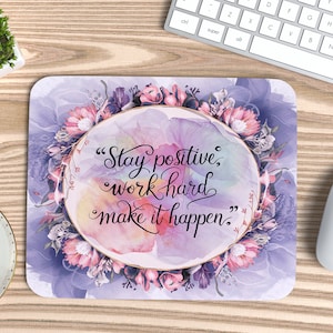 May include: A purple and pink floral design mousepad with a gold circle in the center. The text inside the circle reads "Stay positive, work hard, make it happen."