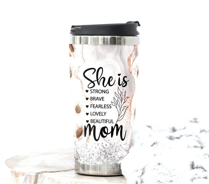 May include: Stainless steel travel mug with a black lid. The mug features a white marble design with gold and silver accents, and small sunflower illustrations. Text on the mug reads "She is STRONG, BRAVE, FEARLESS, LOVELY, BEAUTIFUL mom."