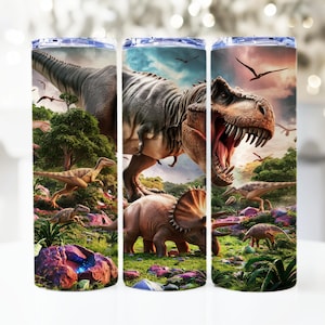 May include: A set of three stainless steel tumblers with a dinosaur theme. The tumblers feature a green, brown, and gray Tyrannosaurus Rex with a bright orange mouth, surrounded by other dinosaurs in a jungle setting.