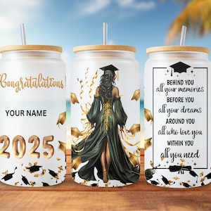 May include: Three white tumblers with gold accents and a graduation theme. The center tumbler features a woman in a green gown and gold cap walking away from the viewer. The left tumbler has the text "Congratulations!" and "2025". The right tumbler has the text "Behind you all your memories, before you all your dreams, around you all who love you, within you all you need".