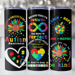May include: Three black stainless steel tumblers with colorful designs and text related to autism awareness. The first tumbler has a sunflower with puzzle pieces and the text "Accept Understand Autism Awareness". The second tumbler has an infinity symbol with puzzle pieces and the text "Society Says I'm Autistic God Says I'm Perfect I Don't Speak Much Because I'm Brilliant And I'm Busy Thinking". The third tumbler has an apple with puzzle pieces and the text "Teach-Hope Love-Inspire Where You Can Be Anything Be Kind".
