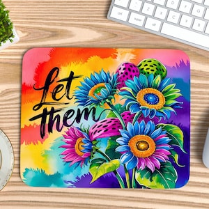May include: A rectangular mousepad featuring a vibrant floral design with sunflowers in shades of blue, pink, and orange. The mousepad has the words "Let them" in black script. The background is a watercolor wash of rainbow colors.