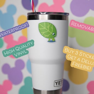 May include: A white Yeti tumbler with a green leaf sticker. The sticker is on the front of the tumbler. Text on the image includes "Waterproof!", "High Quality Vinyl", and "Removable!". The background has colorful Mickey Mouse shapes.