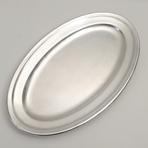 Può includere: Un vassoio ovale e lucido con un bordo rialzato. Il vassoio è realizzato in metallo riflettente color argento. Il design è semplice ed elegante, adatto per servire cibo in un evento formale o per l'uso quotidiano.