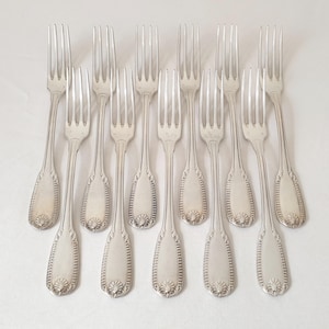 Peut inclure: Dix fourchettes argentées disposées sur une surface blanche. Chaque fourchette présente un long manche fin avec un motif orné à la base. Les dents sont espacées uniformément. Les fourchettes sont toutes orientées dans la même direction.