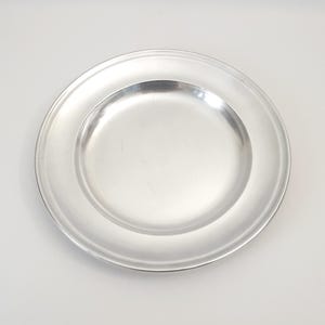 Könnte beinhalten: Ein silberner Teller mit einem erhöhten Rand. Der Teller ist rund und hat eine glatte Oberfläche.