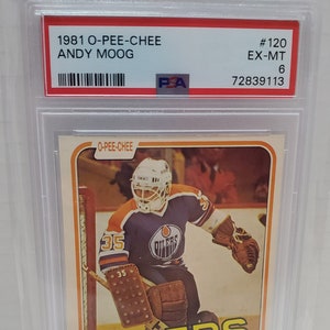 May include: A 1981 O-Pee-Chee hockey card featuring Andy Moog, goalie for the Edmonton Oilers. The card is in excellent condition and graded EX-MT 6 by PSA. The card features a photo of Moog in his Oilers uniform, with the team logo and name prominently displayed.