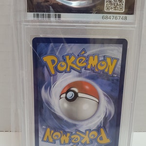 May include: A Pokemon trading card graded by PSA with a blue background and a Pokeball in the center. The card is encased in a clear plastic case with a black label that reads "PSA" and a barcode. The label also includes the number "68476748".