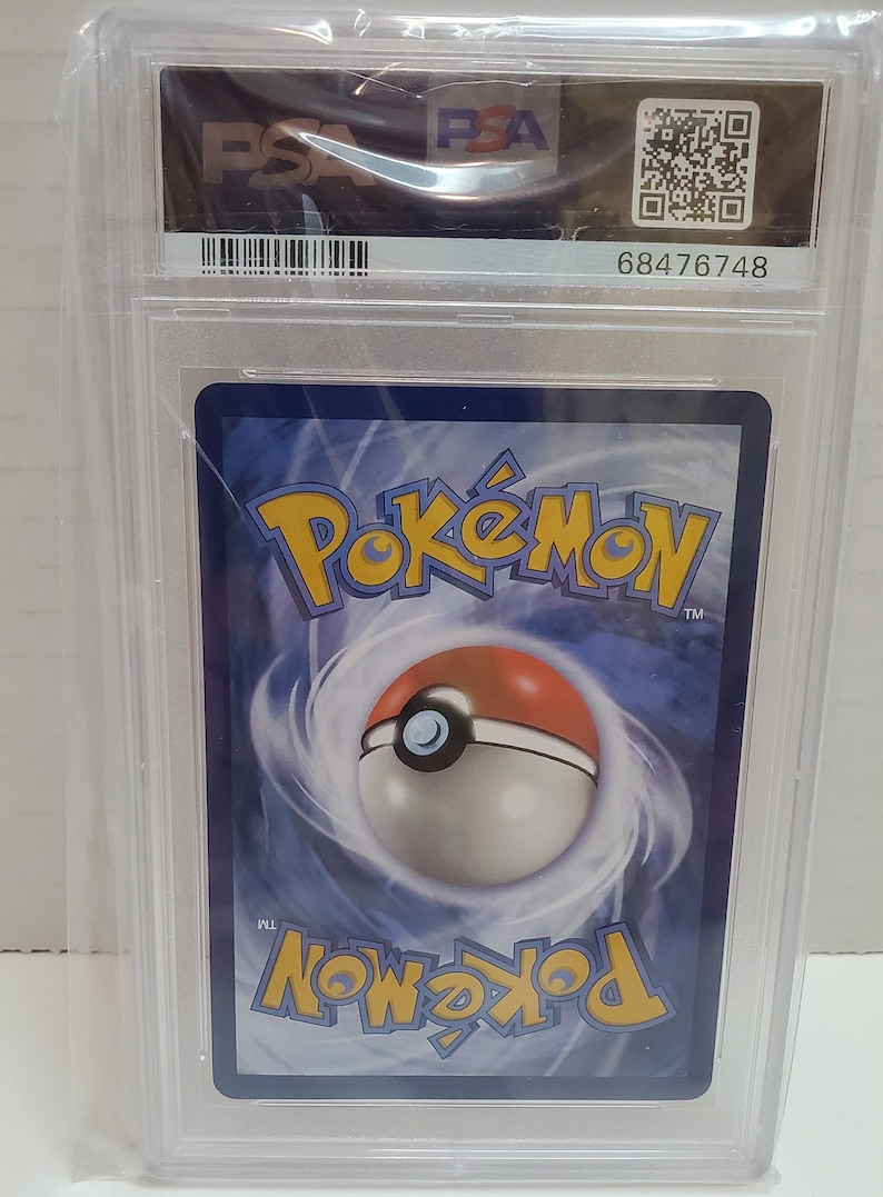 May include: A Pokemon trading card graded by PSA with a blue background and a Pokeball in the center. The card is encased in a clear plastic case with a black label that reads "PSA" and a barcode. The label also includes the number "68476748".