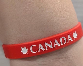 May include: Red rubber wristband with the word "CANADA" in white lettering and a white maple leaf on either side.