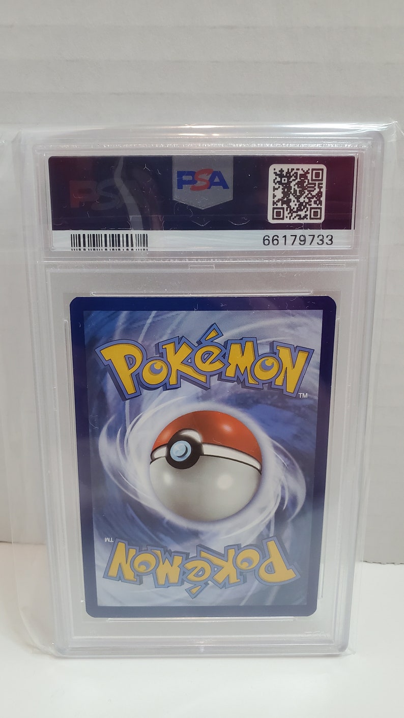 May include: A PSA graded Pokemon card in a clear plastic case with a blue and white border. The card features the Pokemon logo and a Pokeball graphic. The case has a barcode and the number 66179733.