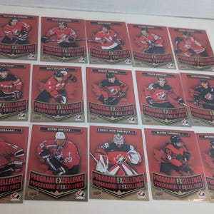 May include: A collection of hockey trading cards featuring players in red and black jerseys. Each card has a red background with the words "Program Excellence" and "Programme D'Excellence". The cards are from the Upper Deck brand.