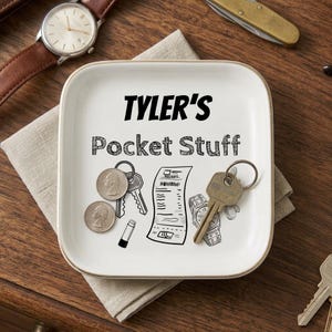 May include: A square white ceramic trinket tray with rounded corners featuring the black printed text TYLER'S Pocket Stuff and black line art illustrations of keys, a receipt, and a watch. Two silver coins and a metal key are resting on the tray.