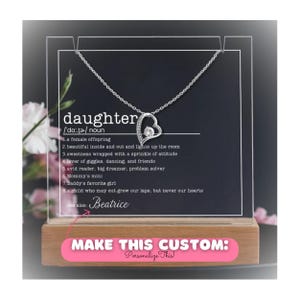 May include: A clear acrylic display box with a silver necklace featuring a heart pendant with a crystal. The box has a wooden base and a pink label that says "MAKE THIS CUSTOM: Personalize This!" The text inside the box reads "daughter /'dɔː.tə/ noun 1. a female offspring 2. beautiful inside and out and lights up the room 3. sweetness wrapped with a sprinkle of attitude 4. lover of giggles, dancing, and friends 5. avid reader, big dreamer, problem solver 6. Mommy's mini 7. Daddy's favorite girl 8. a child who may out grow our laps, but never our hearts see also: Beatrice"