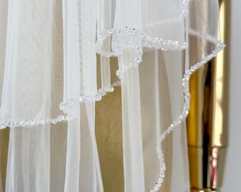 May include: White bridal veil with a beaded edge. The veil is layered and has a delicate, sheer texture.
