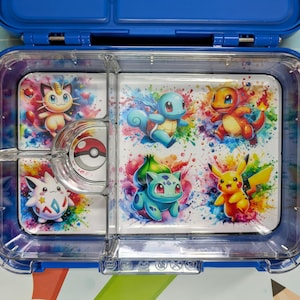 Op de afbeelding: Een doorzichtige lunchbox van plastic met een kleurrijk Pokemon-ontwerp. De lunchbox heeft vier compartimenten en een afneembaar deksel. Het ontwerp toont Pikachu, Squirtle, Charmander en andere Pokemon-personages.