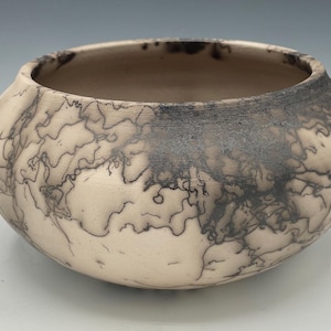 May include: A white ceramic bowl with a black and brown marbled design. The bowl has a round shape and a wide opening.