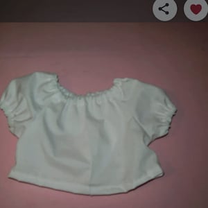May include: A white, short-sleeved top with a gathered neckline and sleeves. The fabric appears to be a lightweight material, possibly cotton or a similar blend. The top has a simple, classic design.