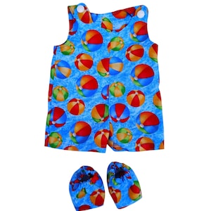 May include: A blue romper and matching booties set, patterned with colorful beach balls. The sleeveless romper has white buttons on the straps. The booties have elastic openings. The fabric has a light blue background.