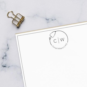 May include: A white notepad with a black circle logo featuring a stethoscope and the initials "C|W" with the text "Conrad Williams II, M.D." below the logo.