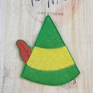 May include: Green and yellow felt elf hat with a red felt feather. The hat is a felt applique.
