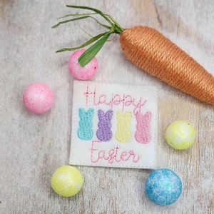 May include: A white felt patch with the text "Happy Easter" and five embroidered pastel-colored bunny shapes. The patch is surrounded by six pastel-colored Easter eggs.