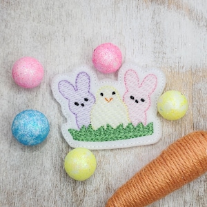 May include: Embroidered felt patch with three pastel Easter bunnies and a chick, surrounded by green grass. The patch is surrounded by pastel-colored Easter eggs.