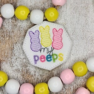 May include: A white felt patch with three embroidered pastel-colored peeps and the text "my peeps" in rainbow colors.