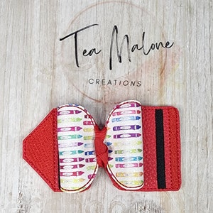 May include: Red fabric hair bow with a crayon pattern and a black elastic band. The bow is tied with a red ribbon.