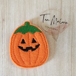 May include: A felt orange pumpkin with a green stem and a black jack-o'-lantern face.