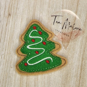 May include: A felt Christmas tree ornament with green felt and white stitching. The tree has red felt ornaments and a white swirl design.
