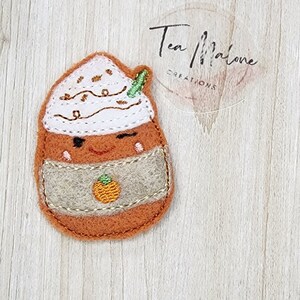 May include: A felt appliqué of a pumpkin spice latte with a winking face and a brown felt cup. The latte has a white whipped cream topping with brown sprinkles and a green straw.