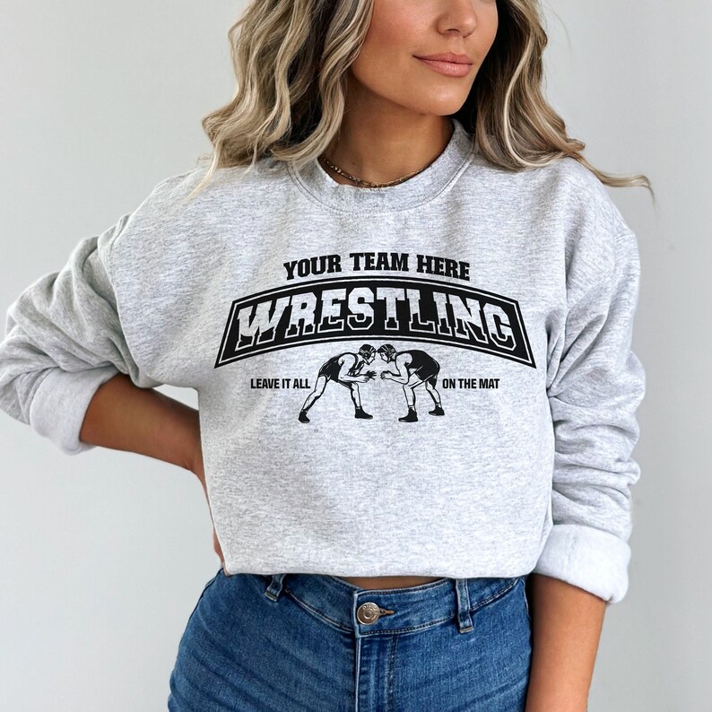 Puede incluir: Sudadera gris con un gr&aacute;fico negro de dos luchadores en una estera. El gr&aacute;fico dice "Your Team Here Wrestling Leave It All On The Mat."