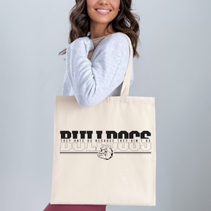 May include: A white canvas tote bag with black text that reads "Bulldogs They Hate Us Because They Ain't Us Bulldogs" with a bulldog graphic.