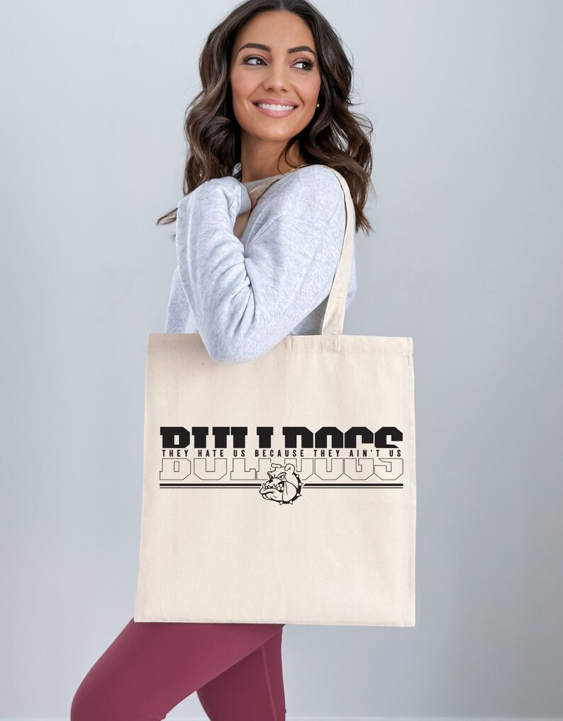 May include: A white canvas tote bag with black text that reads "Bulldogs They Hate Us Because They Ain't Us Bulldogs" with a bulldog graphic.