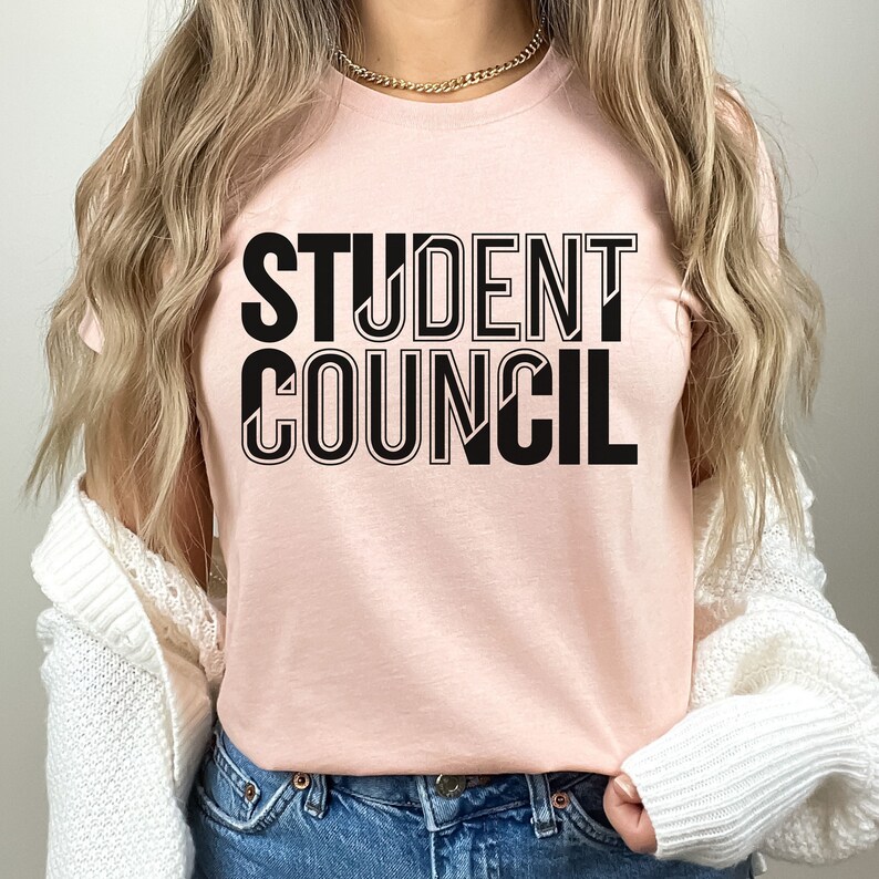 Pu&ograve; includere: Una maglietta rosa con il testo "STUDENT COUNCIL" in lettere nere con contorno.