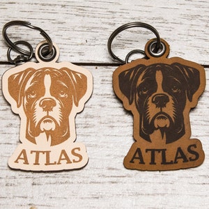 May include: Two leather keychains with a boxer dog silhouette and the name "ATLAS" engraved on each. One keychain is brown and the other is light brown.