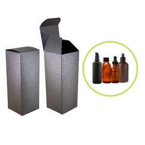 May include: Two tall, rectangular, glittery gray boxes, one open and one closed, are displayed. A green circle contains four different bottles: a black pump bottle, two amber glass bottles, and a brown spray bottle.