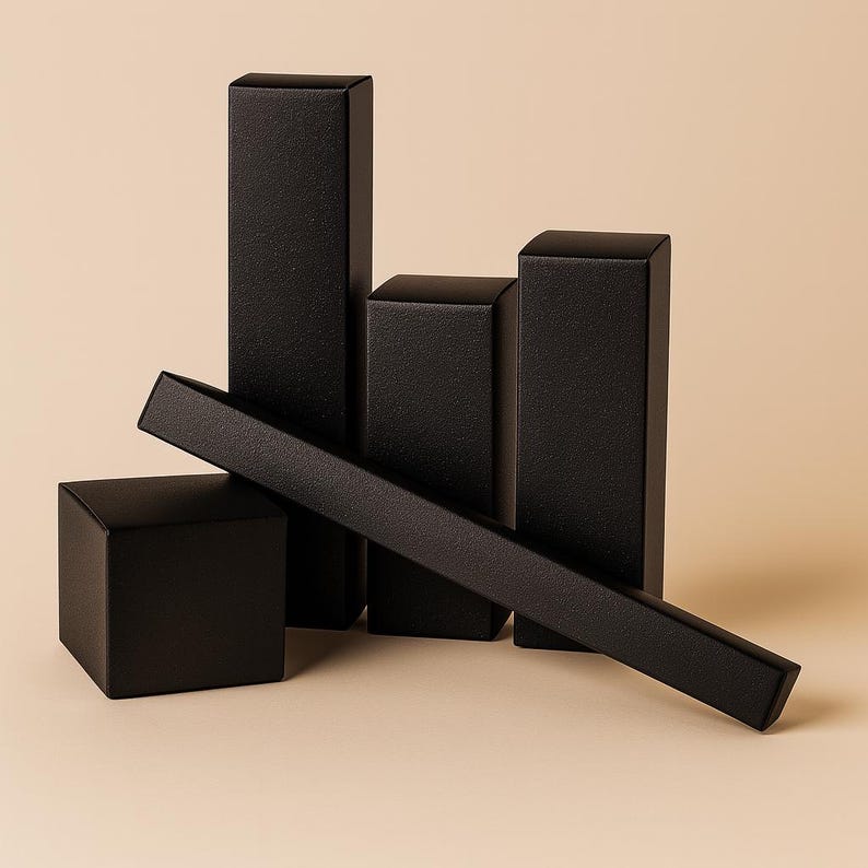 May include: A collection of black, textured rectangular boxes and a long, flat box. The boxes are arranged in a geometric composition against a neutral background. The boxes vary in height and width, creating a visually interesting display.
